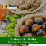 Traditional Bihari dish Litti Chokha served with fresh green chilies and tomatoes, displayed in leaf bowls with branding of The Artery Chronicles